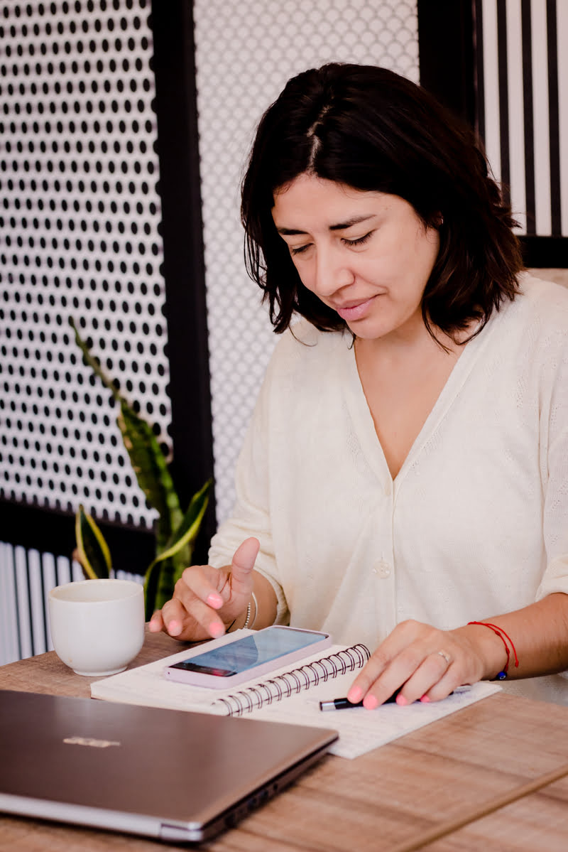 soy mariana taborda mirando el movil sobre una mesa y junto ella un ordenador